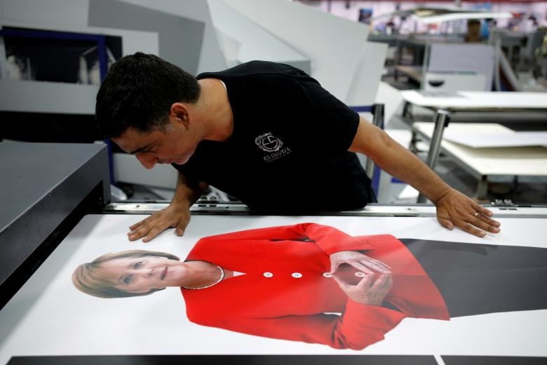 یک کارمند بر روی عکس آنگلا مرکل، صدراعظم آلمان کار می کند