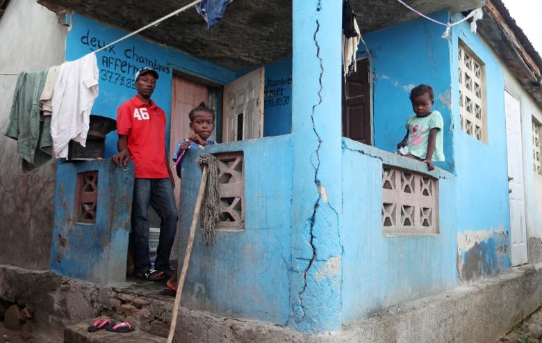 یک مرد با 2 فرزندش بعد از وقوع زمین لرزه هاییتی در ایوان خانه‌شان ایستاده‌اند