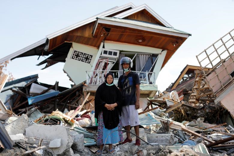 یک خواهر و برادر اندونزیایی در کنار خانه شان در جزیره سولاوسی ایستاده‌اند که در اثر زلزله تخریب شده است