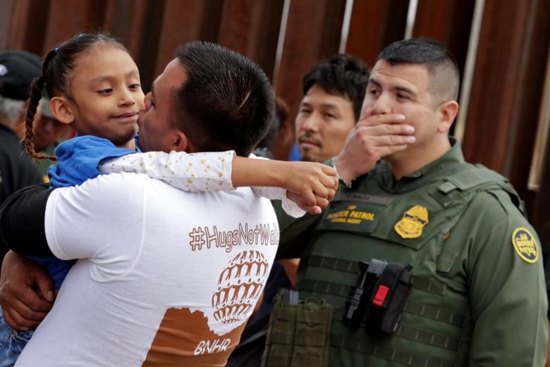 یک مرد کودکی را در مرز مکزیک و آمریکا  در آغوش گرفته است