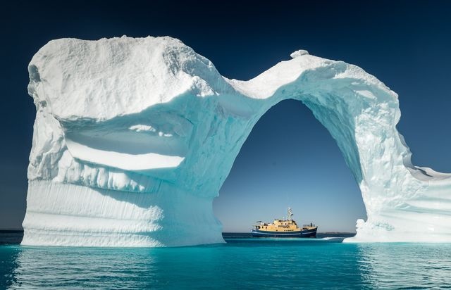 عکس | عبور کشتی از زیر کوه یخی در عکس روز نشنال جئوگرافیک